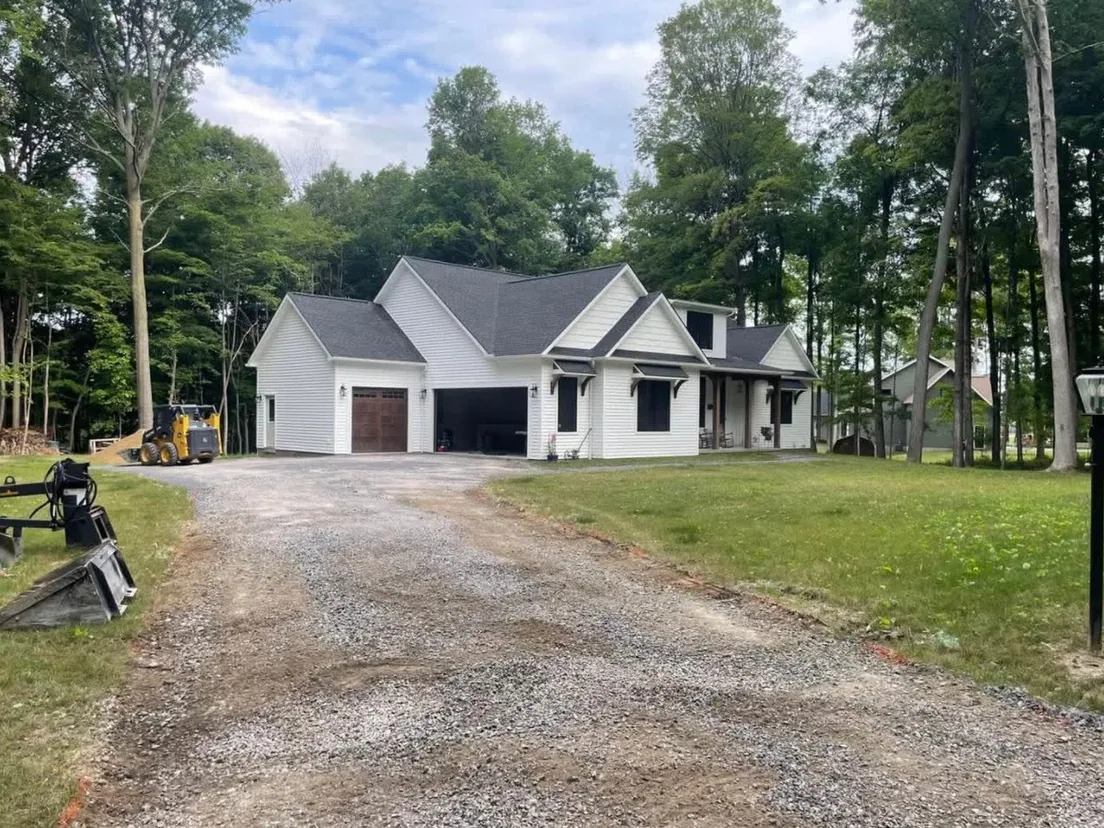 Gravel driveway and skid steer at a white farmhouse before asphalt paving