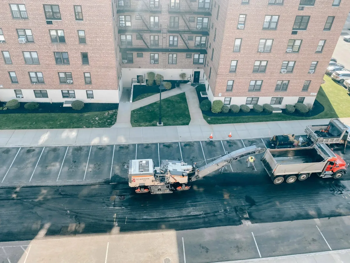 Milling machine grinding old asphalt in an apartment parking lot and loading a dump truck, asphalt milling