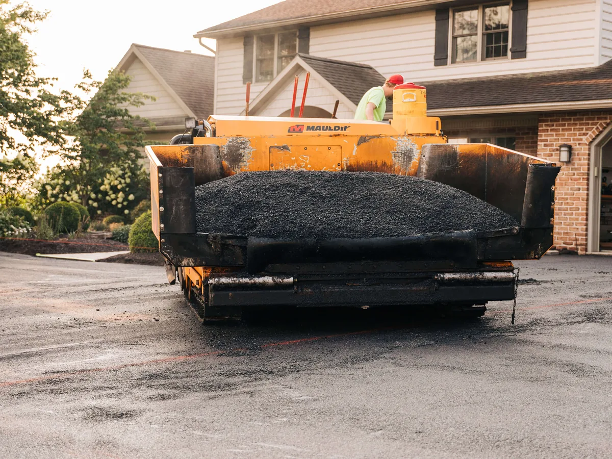 Asphalt paver with a full hopper of hot mix on a home driveway, asphalt resurfacing