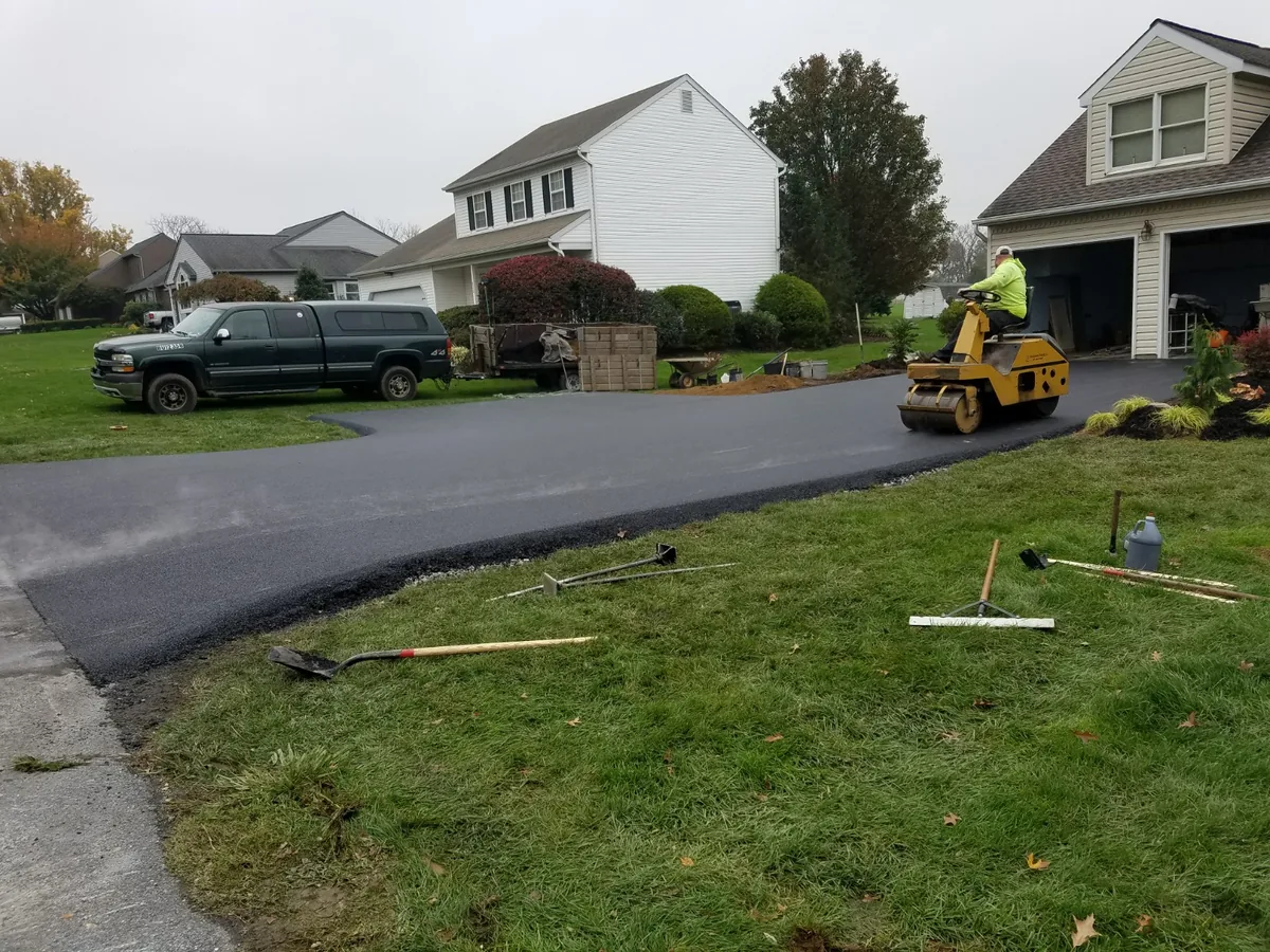 Ride on roller compacting a fresh asphalt driveway beside a house, asphalt resurfacing