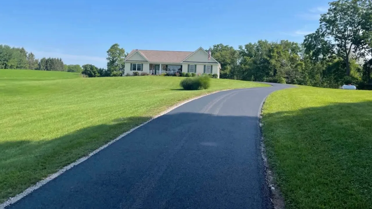 Long asphalt driveway climbing a grassy hill to a ranch house, asphalt paving