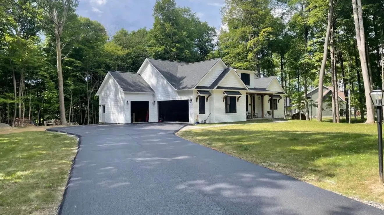 New asphalt driveway curving up to a white farmhouse with a two car garage, asphalt paving