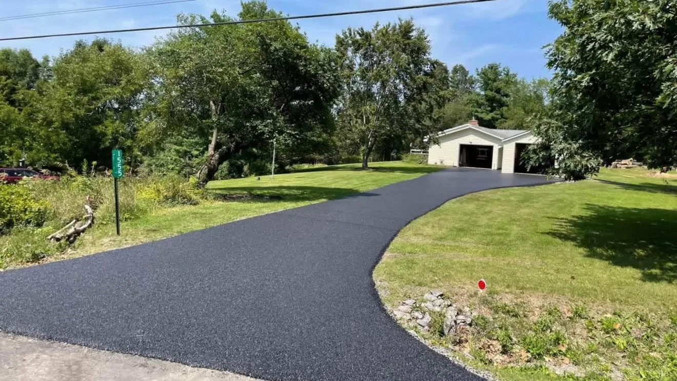 New asphalt driveway curving to a detached garage under trees, asphalt paving