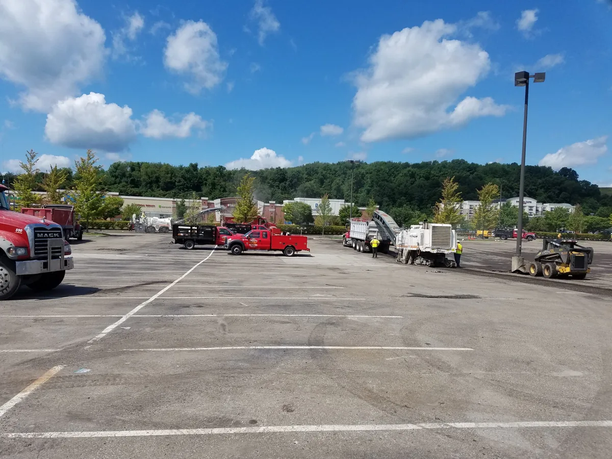 Milling machine loading a dump truck on an old retail plaza parking lot, parking lot paving