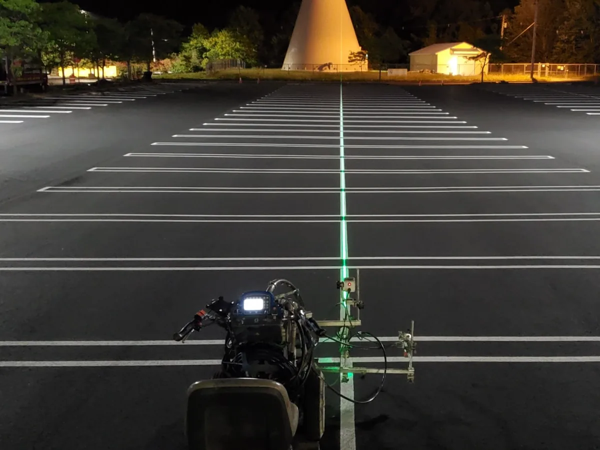 Striping machine painting white stall lines on a dark asphalt parking lot at night, parking lot paving