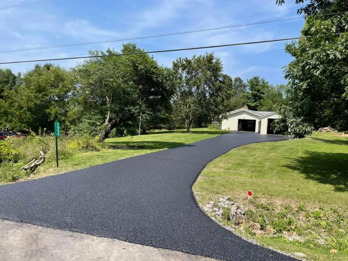 New asphalt drive curving from the road to a detached garage under trees, private road paving
