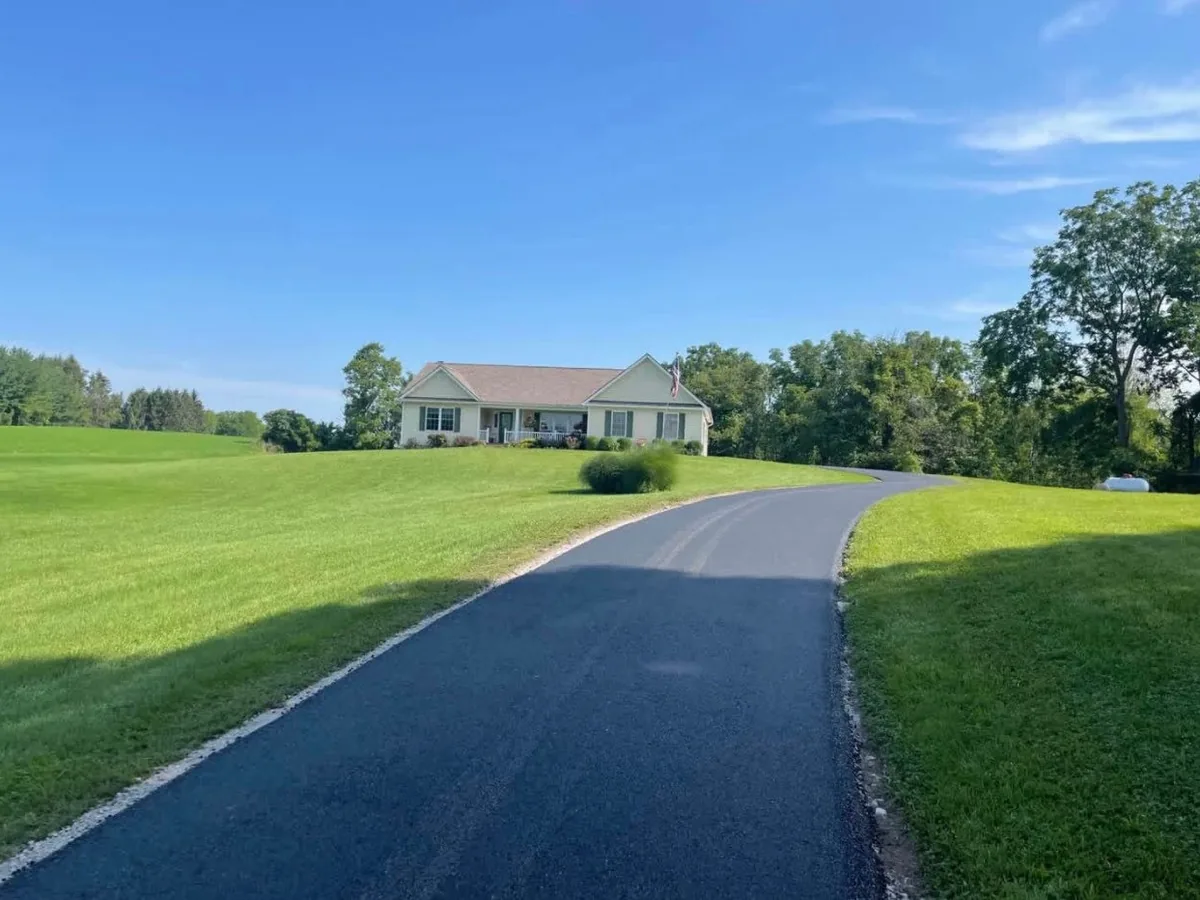 Long asphalt lane climbing a grassy hill to a ranch house, private road paving