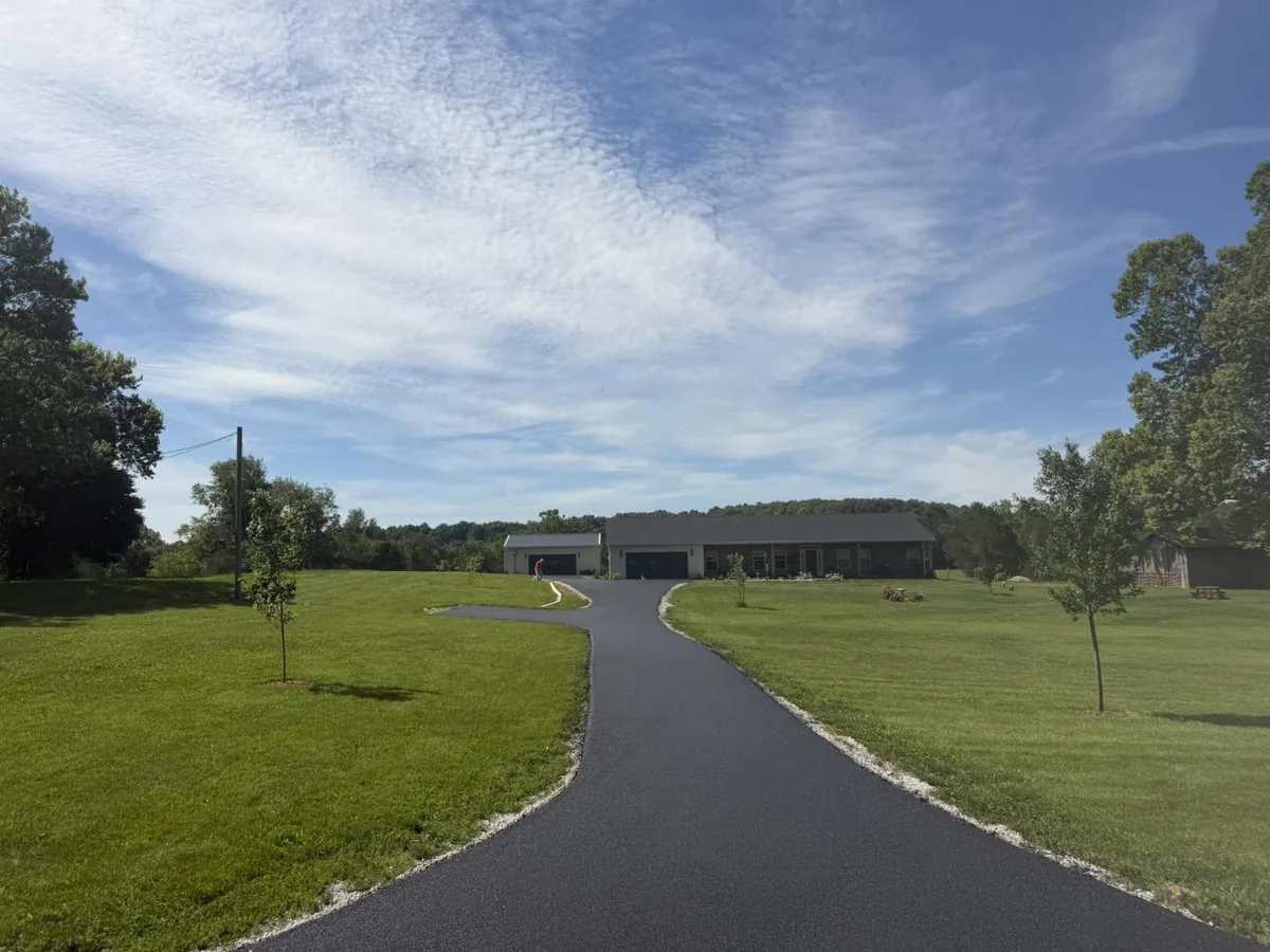 Long new asphalt lane running across open lawn to a home and garage, private road paving
