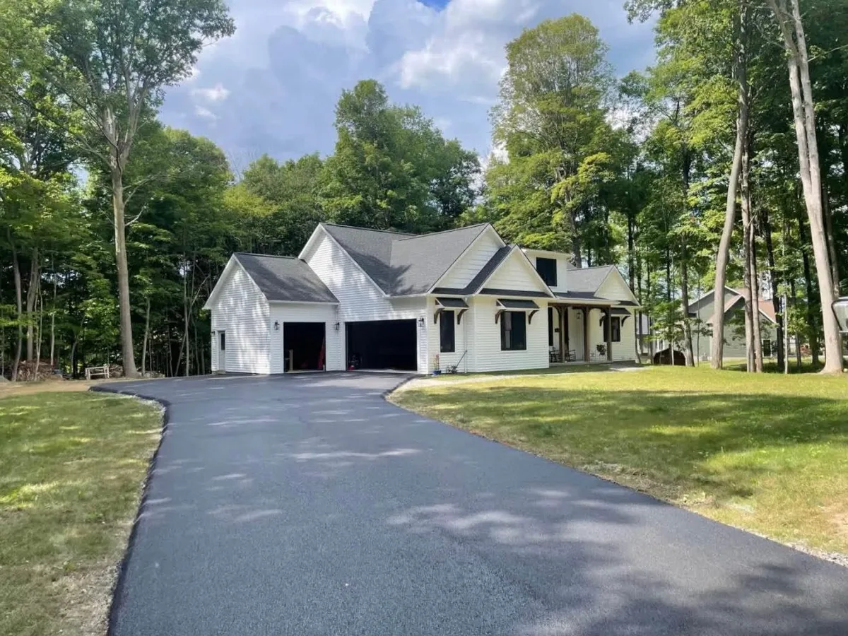 Black asphalt driveway curving up to a white farmhouse, sealcoating