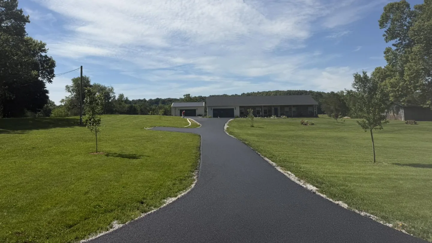 Long new asphalt driveway across a wide lawn under a big sky, asphalt paving
