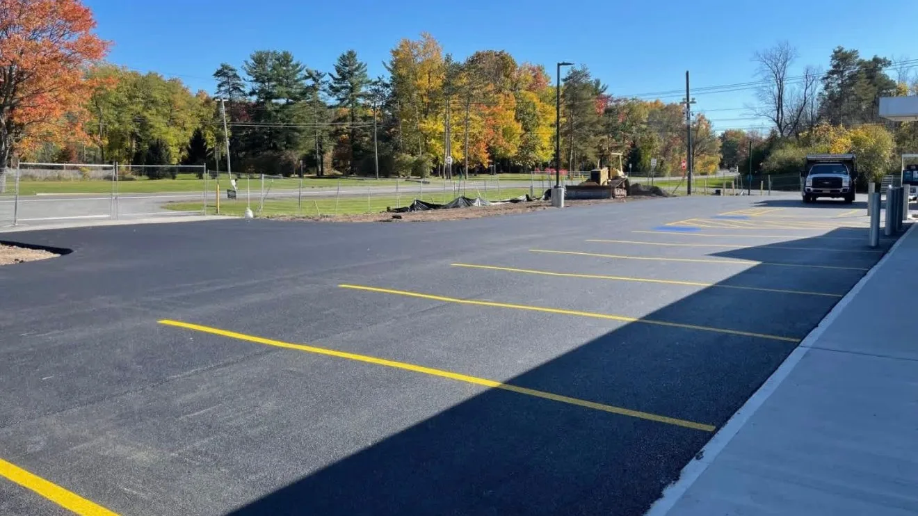 New asphalt parking lot with fresh yellow stall lines under fall trees, asphalt paving services